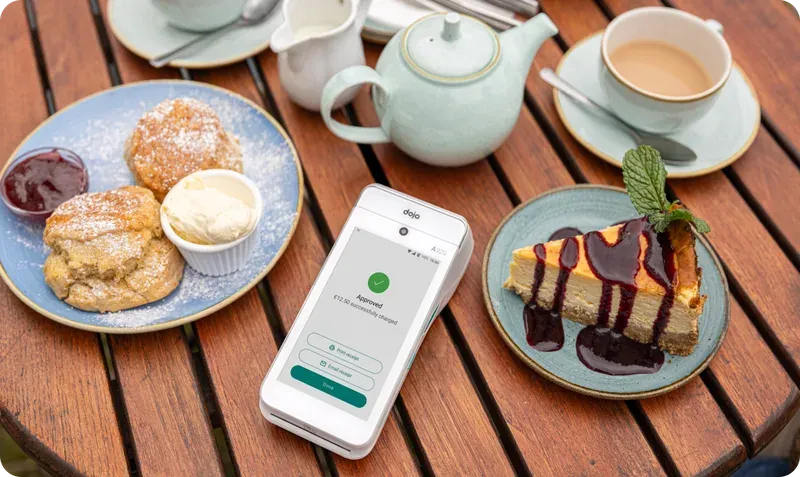 A Dojo card machine on a café table beside tea and scones